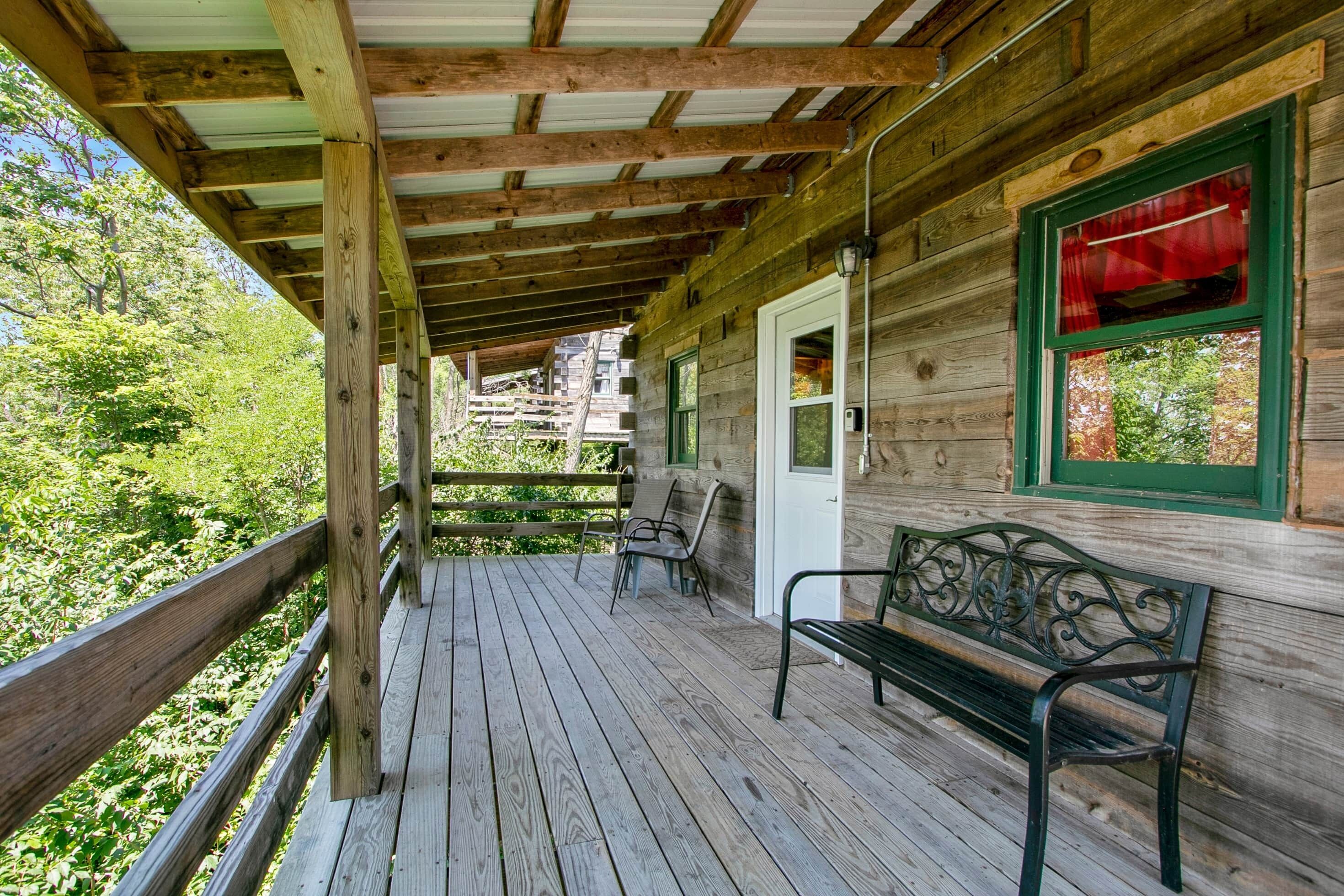 A wooden porch with a bench and chairs, a door with a red curtain, and a view of greenery.