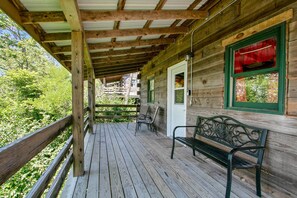Een houten veranda met een bank en stoelen, een deur met een rood gordijn, en uitzicht op groen.