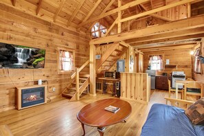 Ein Holzblockhaus-Interieur mit Kamin, Essbereich, Küche und einer Treppe.