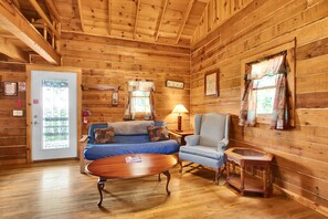 Ein Holzblockhaus-Interieur mit Holzboden, einer Couch, einem Sessel, einem kleinen Tisch und einer Tür mit Fenster.