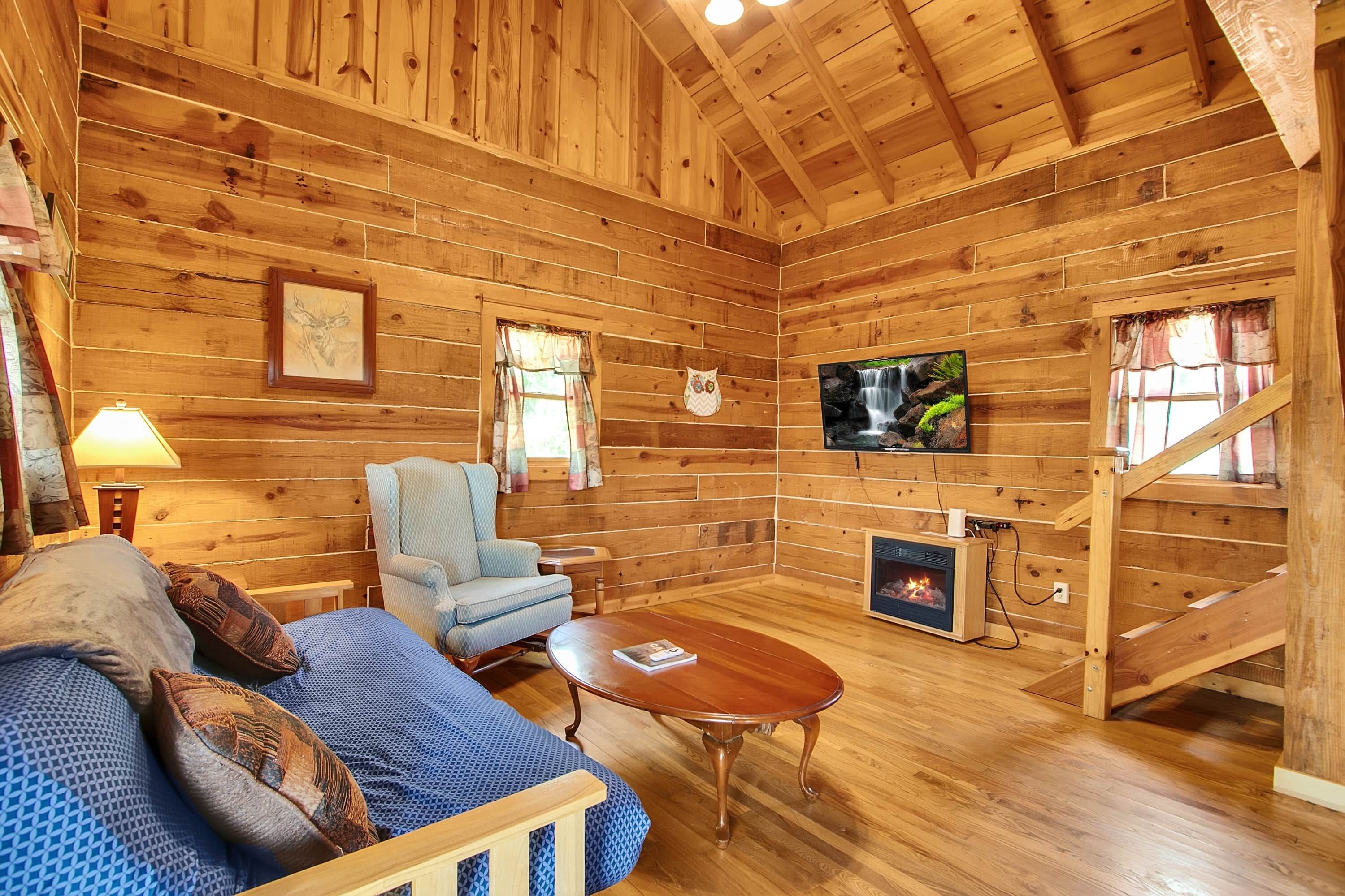 Ein Holzblockhaus-Interieur mit einer Couch, einem Sessel, einem Kamin, einem Fernseher und einem Fenster mit Vorhängen.