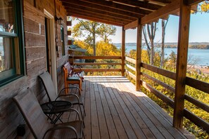 Eine Holzterrasse mit Bank und Stühlen mit Blick auf ein Gewässer und Bäume.
