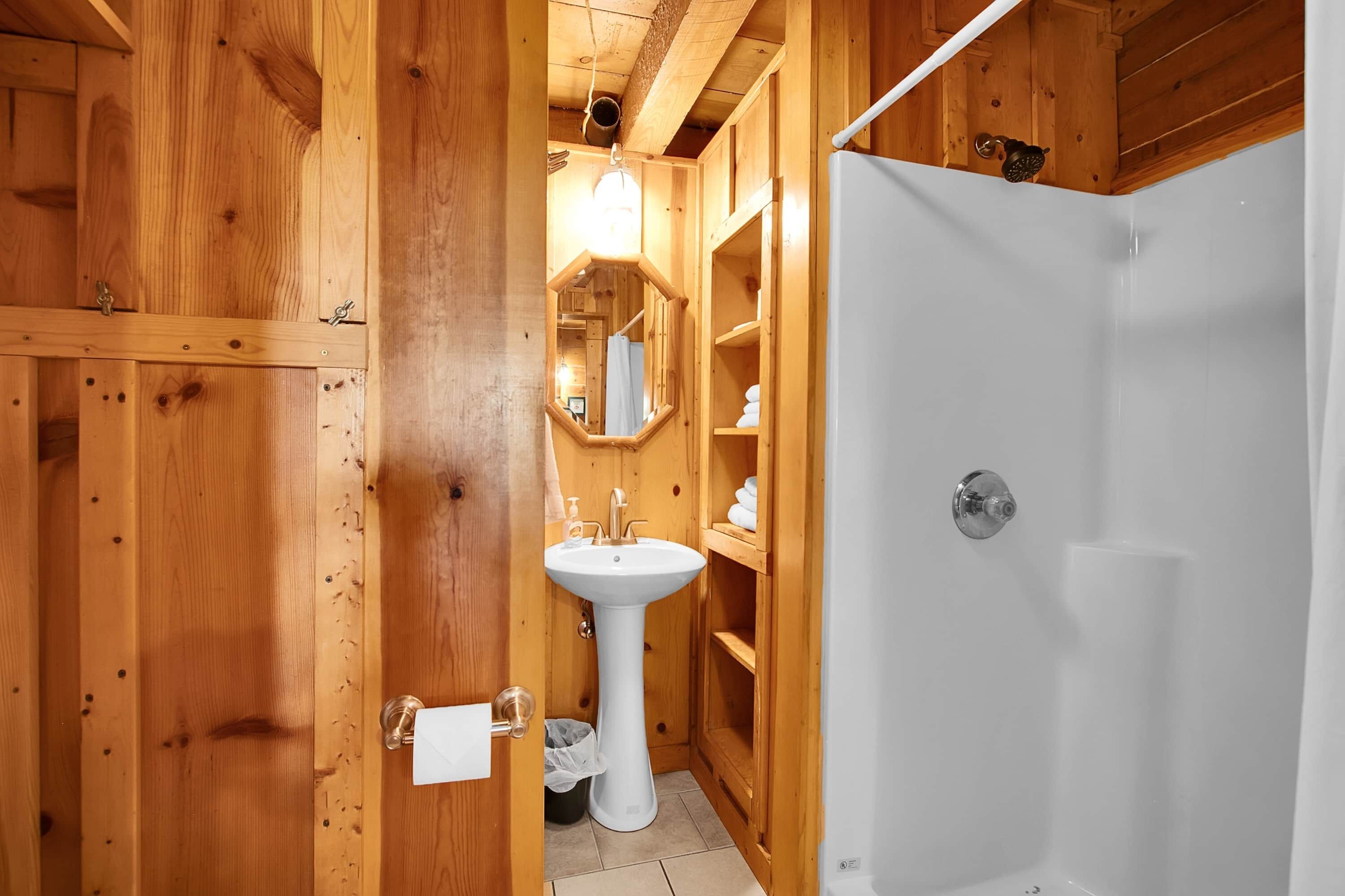 Ein Badezimmer aus Holz mit einem Standwaschbecken, einem Spiegel und einer Dusche.