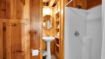 Ein Badezimmer aus Holz mit einem Standwaschbecken, einem Spiegel und einer Dusche.