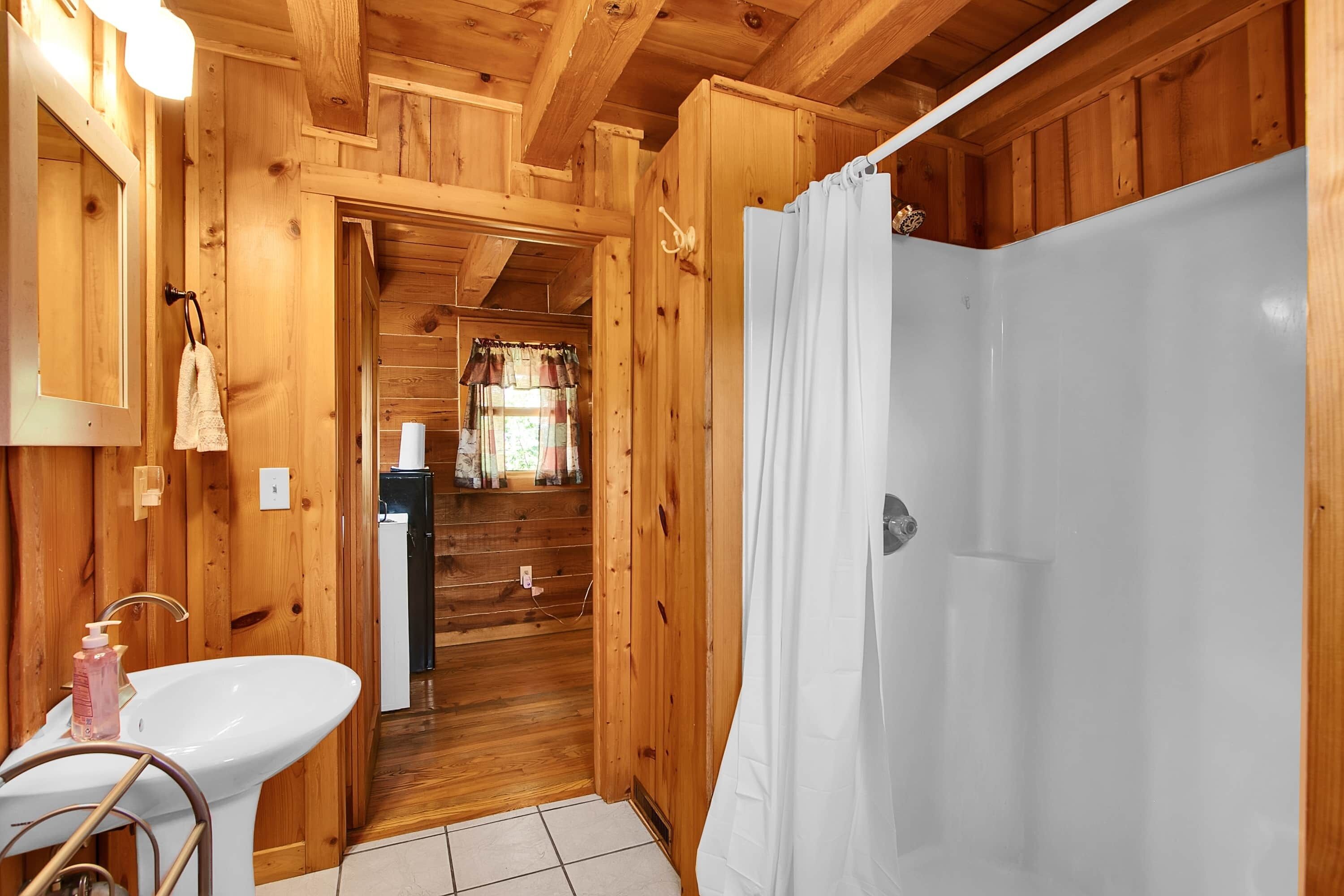 A wooden interior with a white sink, a shower curtain, and a wooden door leading to a bathroom.