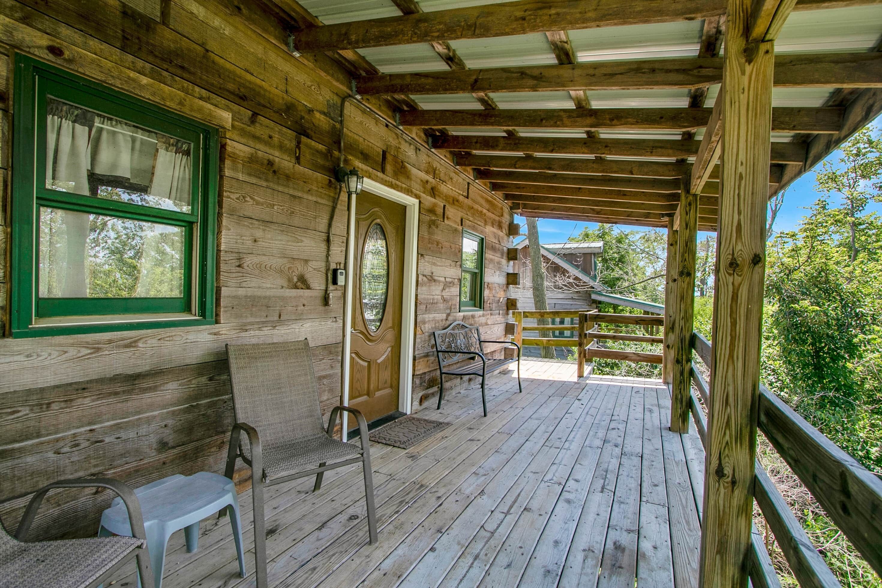 A wooden cabin with a porch, a bench, a chair, and a small table.
