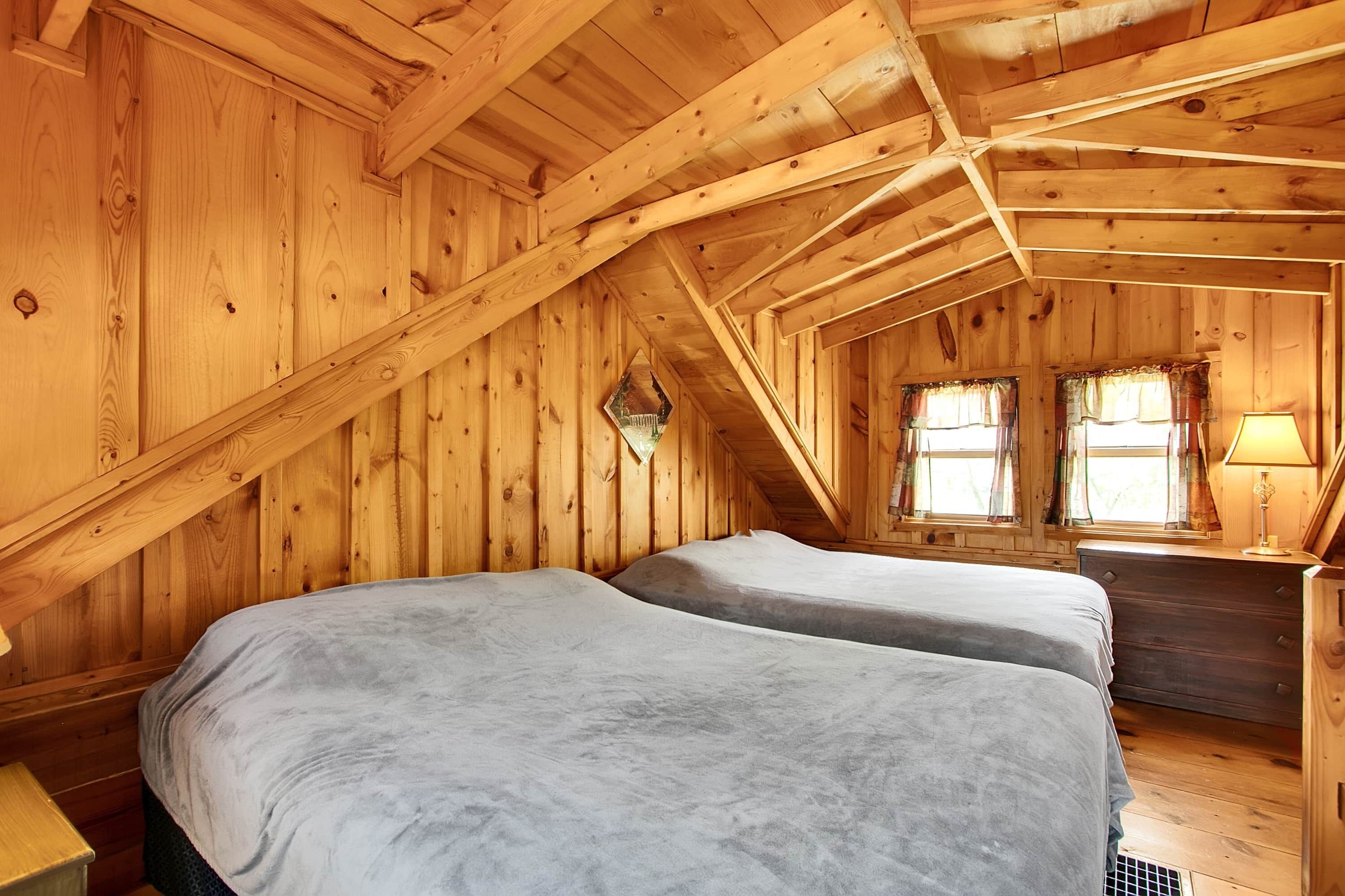 Un dormitorio de cabaña de madera con dos camas, un aparador y una ventana con cortinas.
