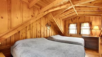 Un dormitorio de cabaña de madera con dos camas, un aparador y una ventana con cortinas.