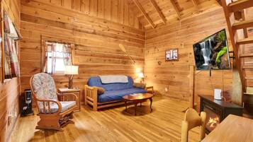 A cozy cabin interior with a wooden floor, a sofa, a rocking chair, a television, and a fireplace.