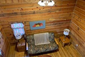 Ein Holzhütten-Interieur mit einem Bett, einem kleinen Tisch, einer Lampe und einem Bild an der Wand.