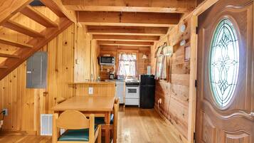 A wooden cabin interior with a dining area, kitchen, and a large window with a decorative glass design.