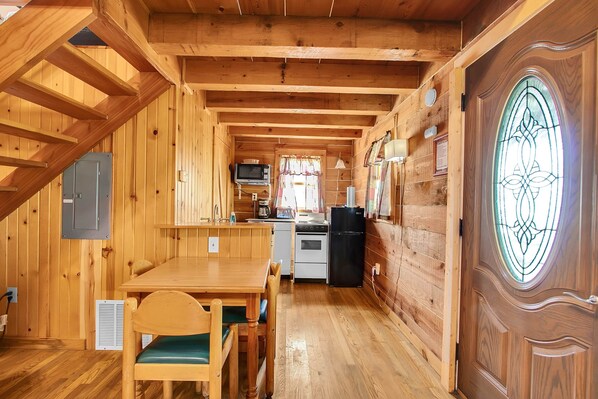 A wooden cabin interior with a dining area, kitchen, and a large window with a decorative glass design.