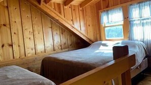 Uma cabana de madeira com teto inclinado, uma cama de solteiro e uma janela com cortinas.