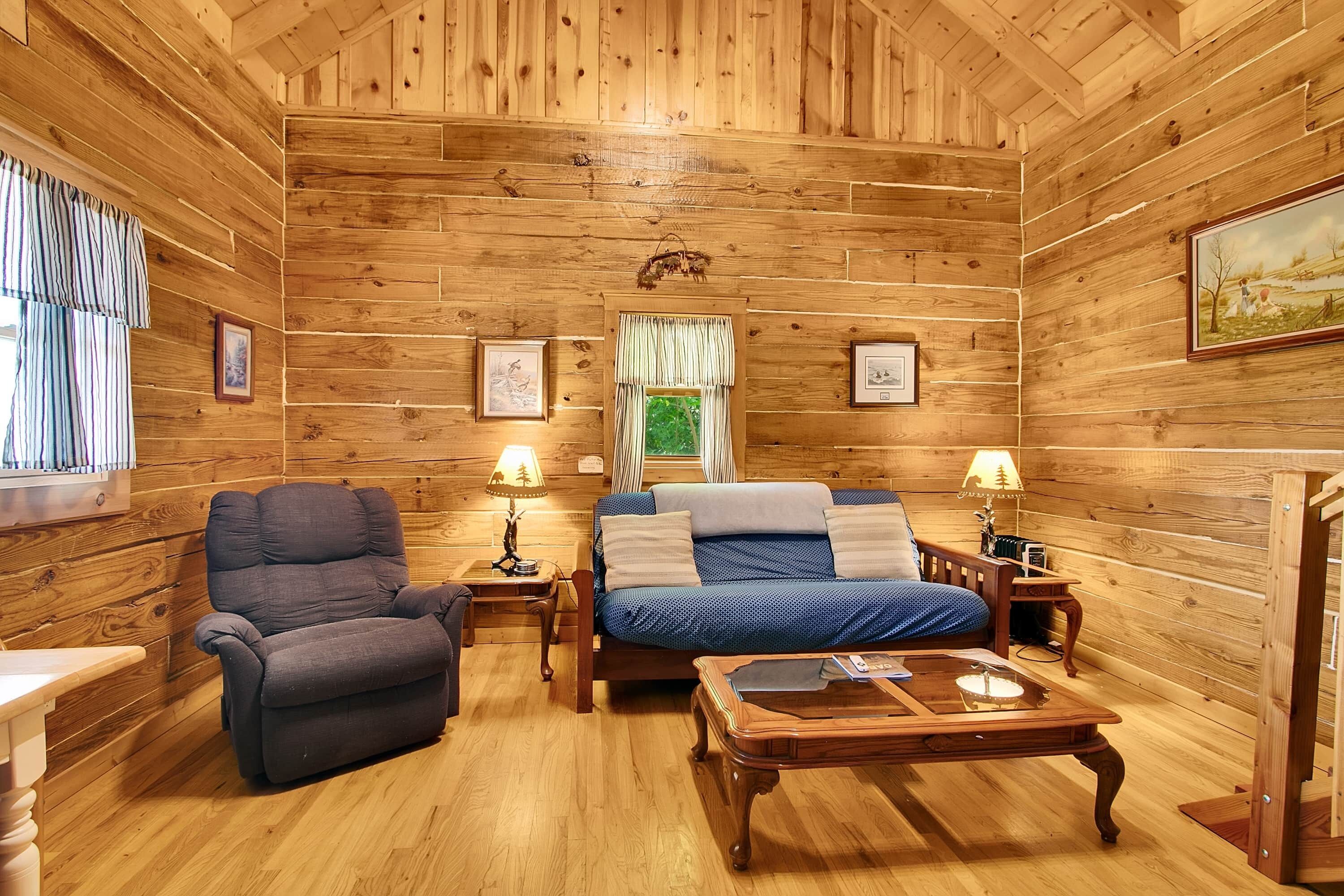 A log cabin interior with a sofa, a bed, a wooden coffee table, and a chair.