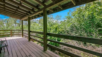 A wooden deck with a railing, surrounded by dense greenery and trees.