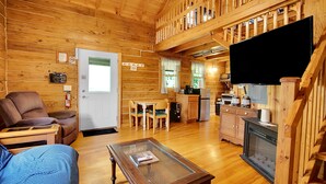 Un intérieur de chalet chaleureux comprenant un salon, un coin repas, une cuisine et une cheminée.