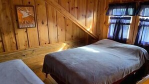 Une cabane avec deux lits, des murs en bois et une fenêtre avec des rideaux.