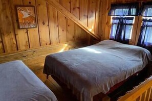 Een chalet met twee bedden, houten wanden en een raam met gordijnen.