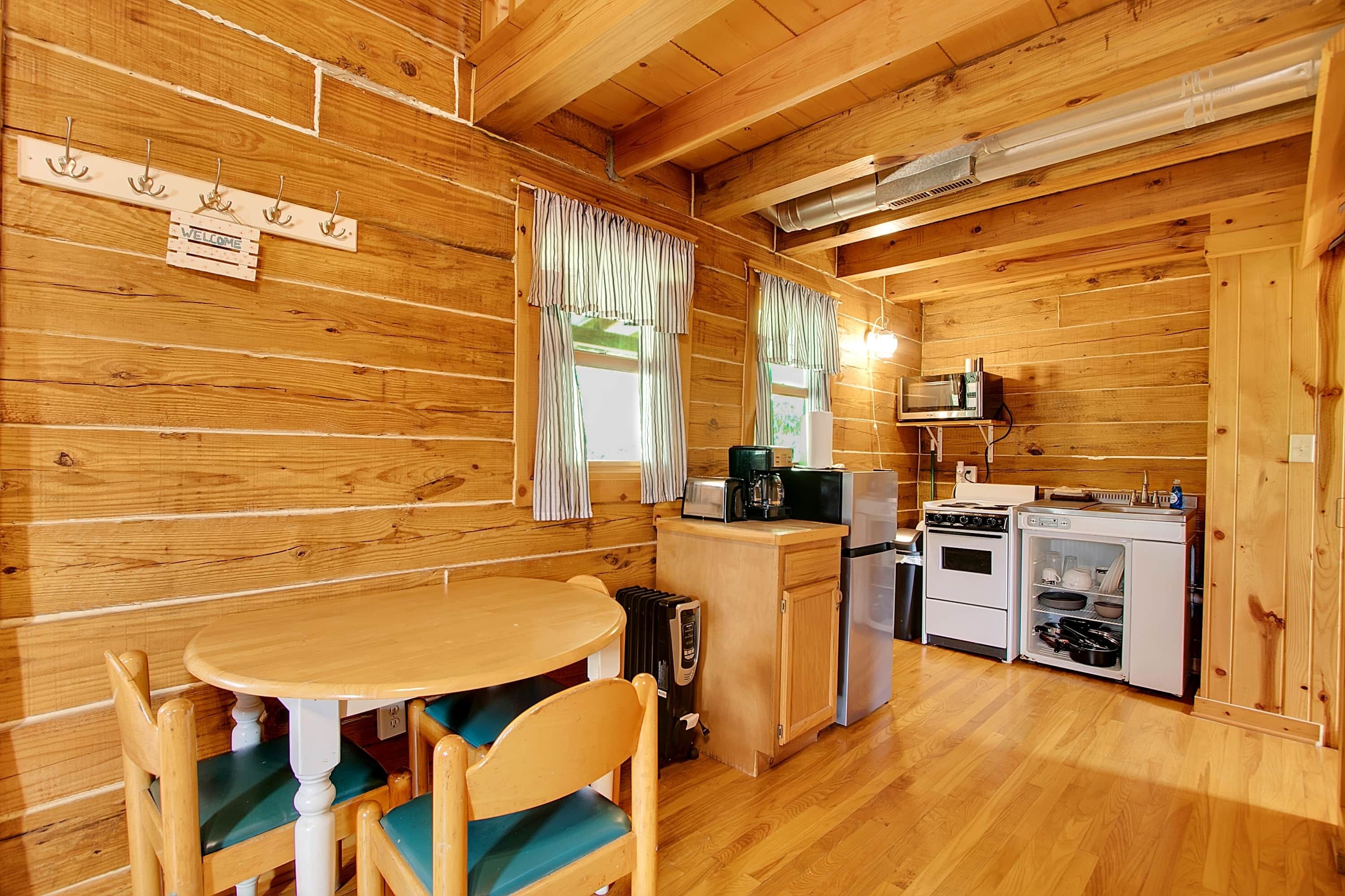 L’intérieur d’une cabane en bois comprend une table à manger, des chaises et un coin cuisine équipé d’une cuisinière, d’un four à micro-ondes et d’un réfrigérateur.