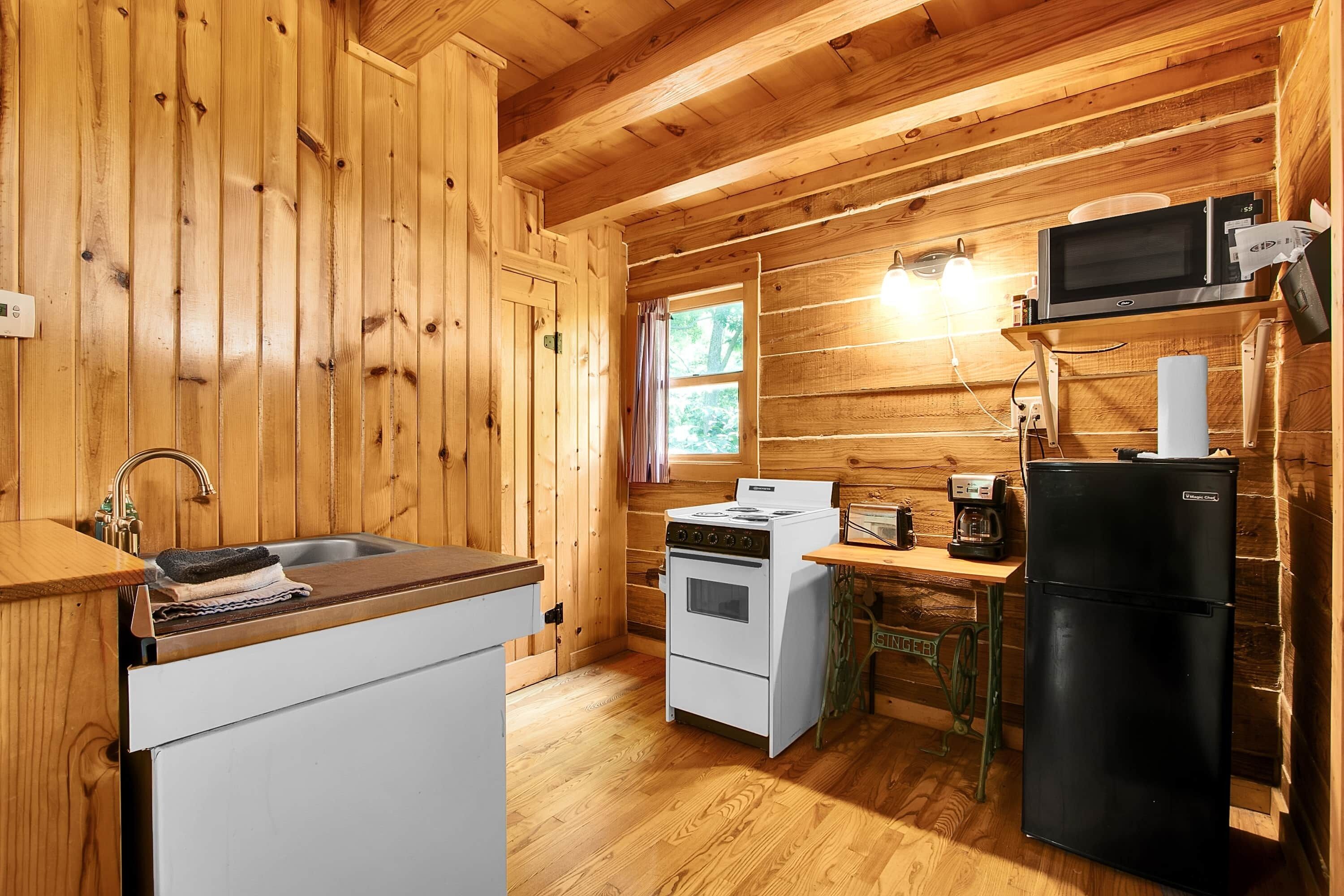 A wooden cabin interior with a kitchen area featuring a stove, refrigerator, and microwave.