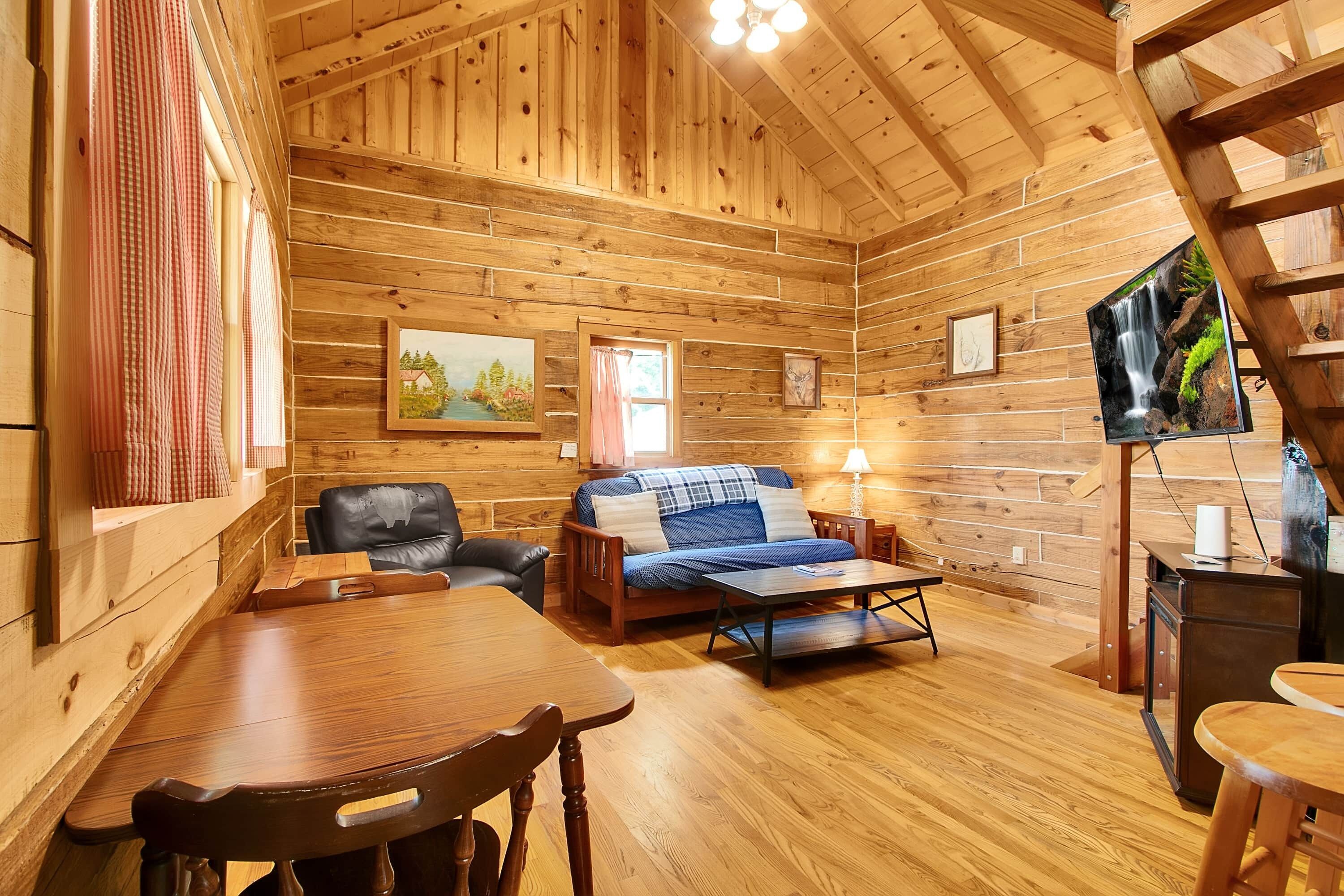 A cozy cabin interior with a wooden interior, a sofa, a dining table, and a television mounted on the wall.