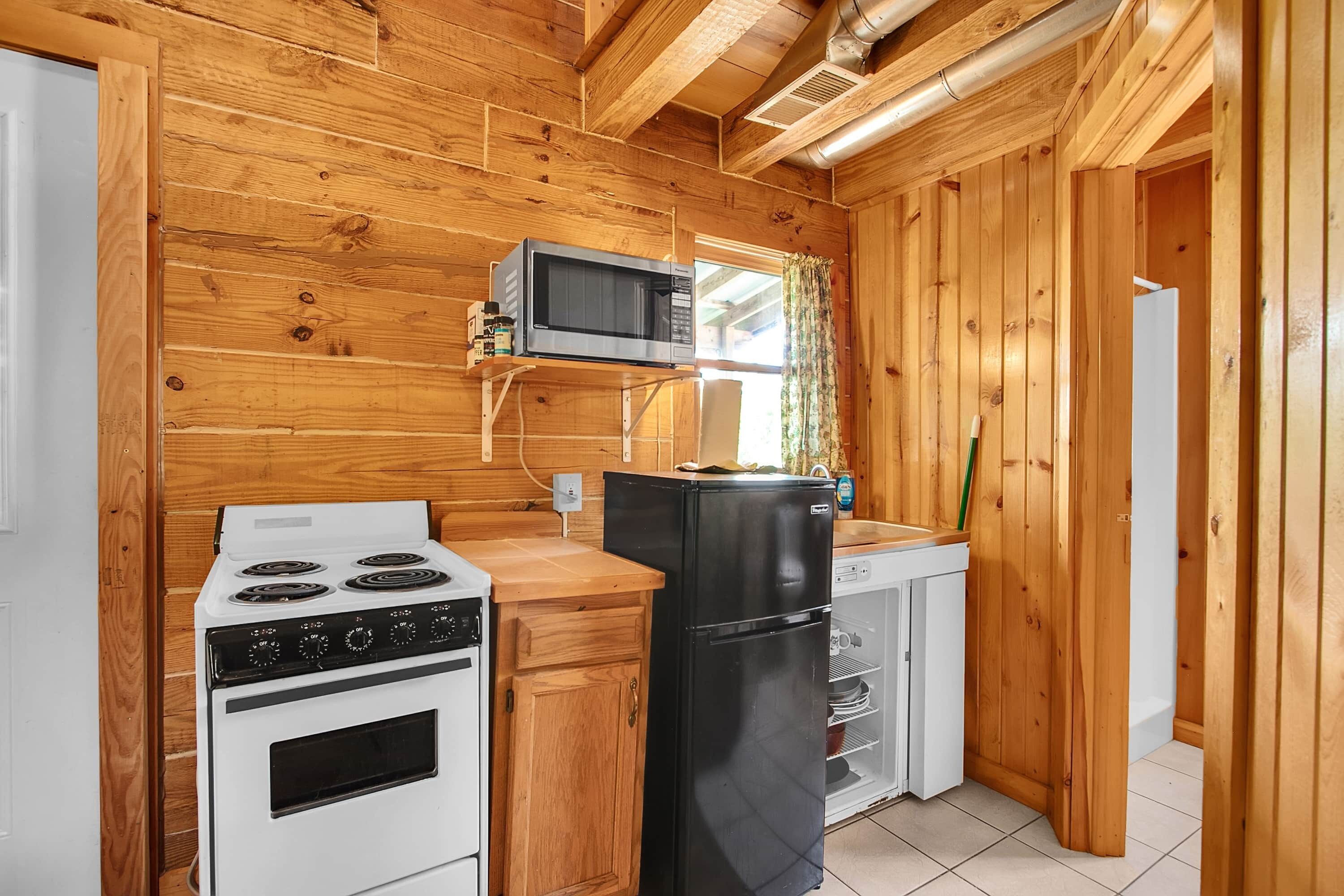 Una cocina compacta con paredes de madera, un microondas, una estufa y un refrigerador.