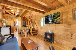 A wooden cabin interior with a fireplace, a television mounted on the wall, a dining area, and a staircase.