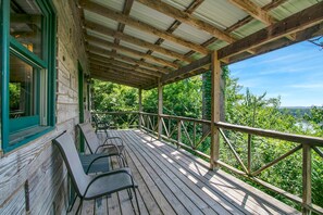 A wooden deck with metal chairs, a covered area with a metal roof, and a view of greenery and a river.