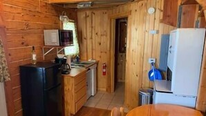 Cocina compacta con paredes de madera, un refrigerador negro, un microondas, un lavamanos y un pequeño cubo de basura.