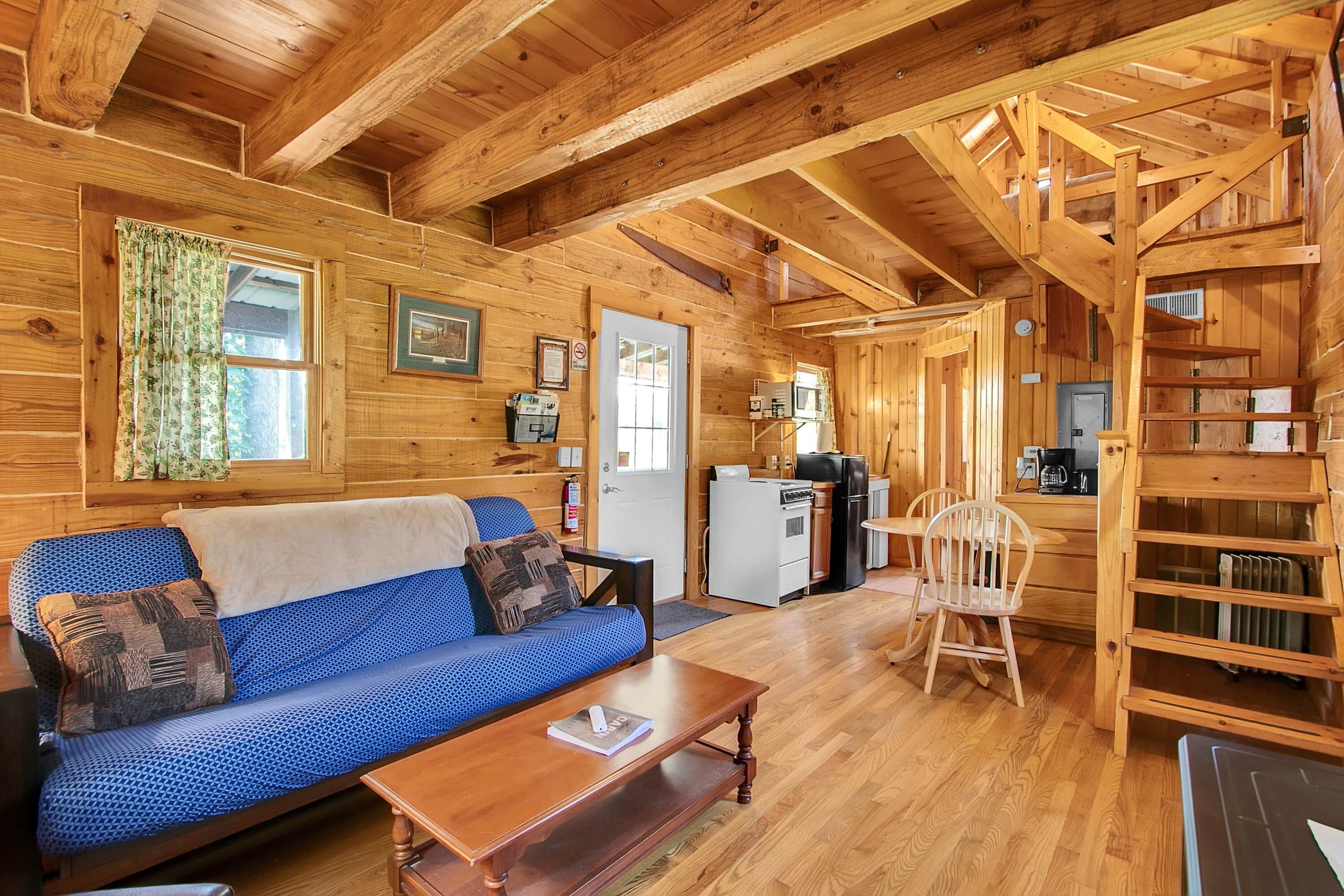 L’intérieur chaleureux d’un chalet avec un plafond en bois, un canapé, une table à manger et un coin cuisine.
