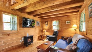 Interior acogedor de una cabaña con chimenea, paredes de madera, un sofá y un televisor montado en la pared.