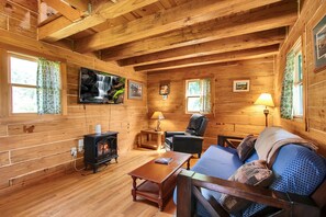 Et hyggeligt sommerhusinteriør med pejs, trævægge, en sofa og et fjernsyn ophængt på væggen.