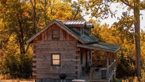 Una cabaña rústica con un porche, una parrilla y una mesa con sillas.