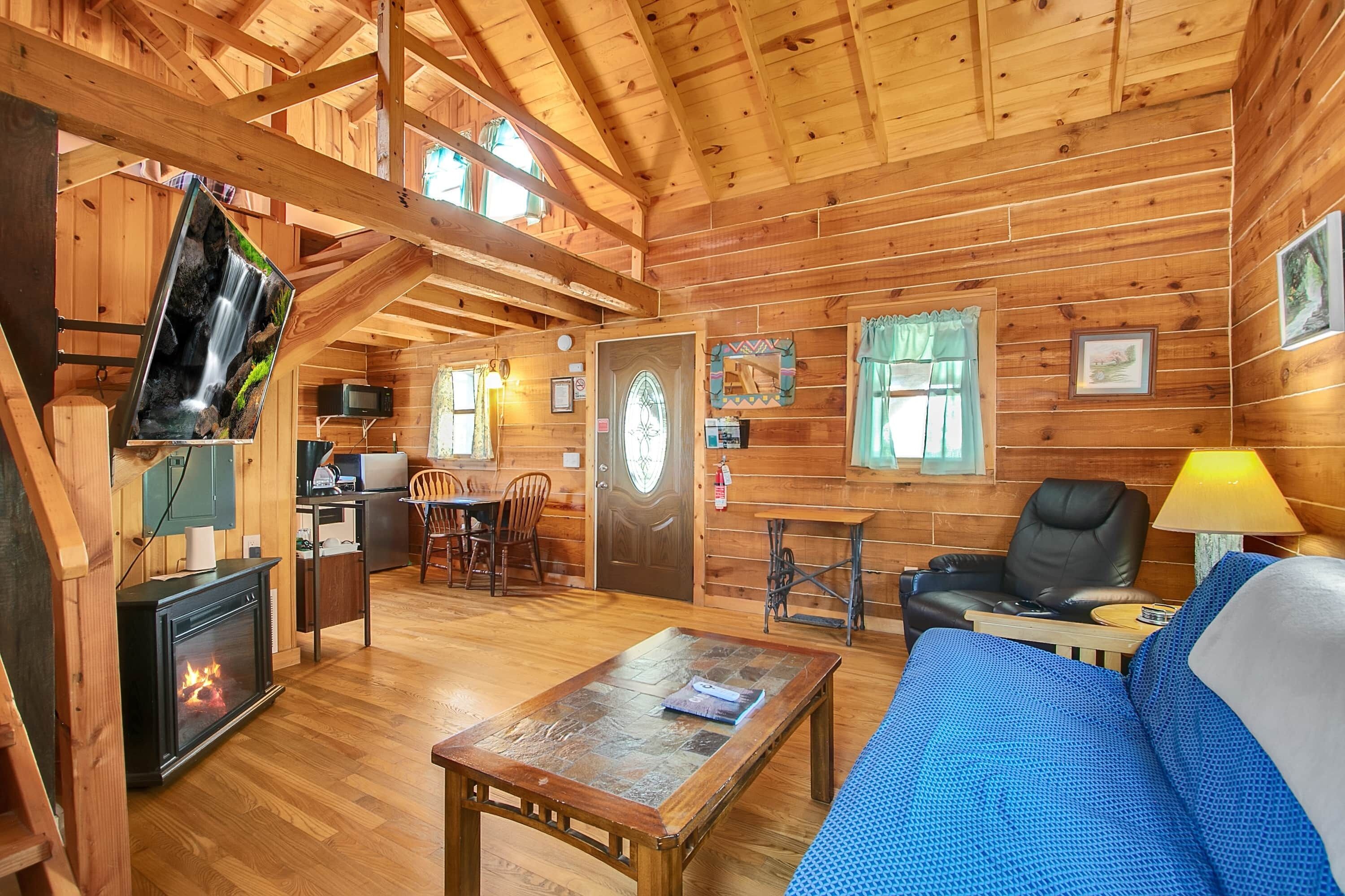 A wooden cabin interior with a fireplace, a sofa, a dining table, and a television.