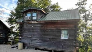 Une cabane rustique en rondins de bois, avec un toit en métal, un petit porche et une fenêtre.
