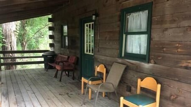 Une cabane en bois avec une véranda, deux chaises en bois et un banc.