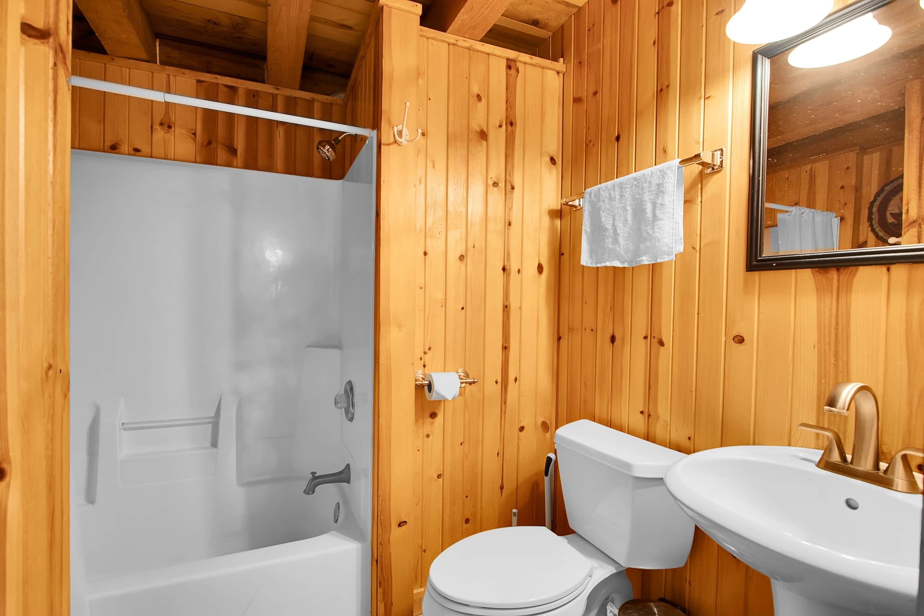 Un baño con paneles de madera, una bañera, un inodoro, un lavamanos y un espejo.