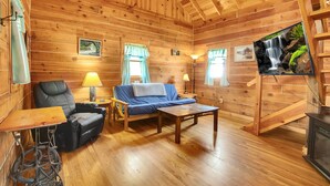 L’intérieur d’un chalet en bois comprend un canapé, un fauteuil, une table et un téléviseur fixé au mur.