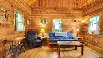 L’intérieur d’un chalet accueillant, avec un plafond en bois, un fauteuil en cuir noir, un canapé bleu et une petite table.