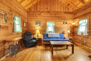 Interior acogedor de una cabaña con techo de madera, un sillón de cuero negro, un sofá azul y una pequeña mesa.