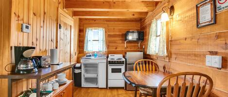 A compact kitchen with a microwave, stove, and refrigerator, wooden walls, and a dining table with chairs.