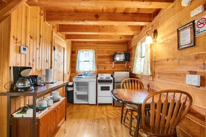 A compact kitchen with a microwave, stove, and refrigerator, wooden walls, and a dining table with chairs.