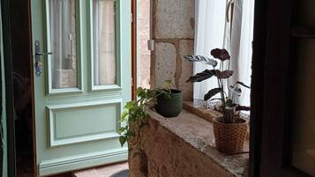 Un arc en pierre mène à une porte dotée d’un cadre vert et surmontée d’un petit seuil. Des plantes en pot sont disposées sur le rebord en pierre au-dessus de la porte.