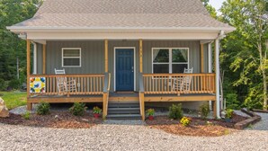 A two-story house with a front porch, a blue door, and a small garden area with potted plants. - Bluebird Cabin | WiFi & River Access (Elkin)