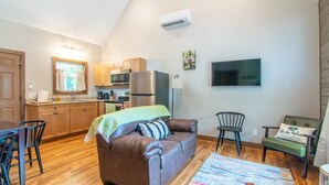 Un espacio habitable compacto con kitchenette, un sofá de cuero marrón, una mesa de comedor y un televisor montado en la pared.