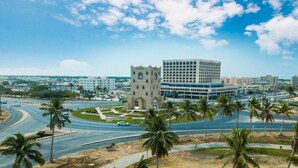 A cityscape with a prominent tower-like structure, a modern building, and palm trees. - Haffa House  (Salalah)