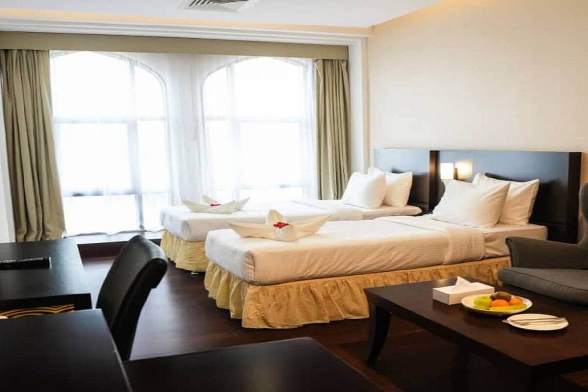 A hotel room with two beds, a sofa, a desk, and a dining table.