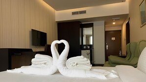 A hotel room with a bed, a television on the wall, a green chair, and a door leading to another room. - Haffa House  (Salalah)