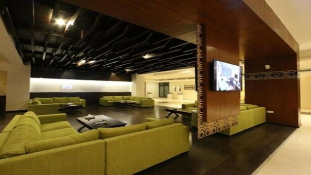 A modern lobby with green sofas, a flat-screen TV, and a patterned wall design. - Haffa House  (Salalah)