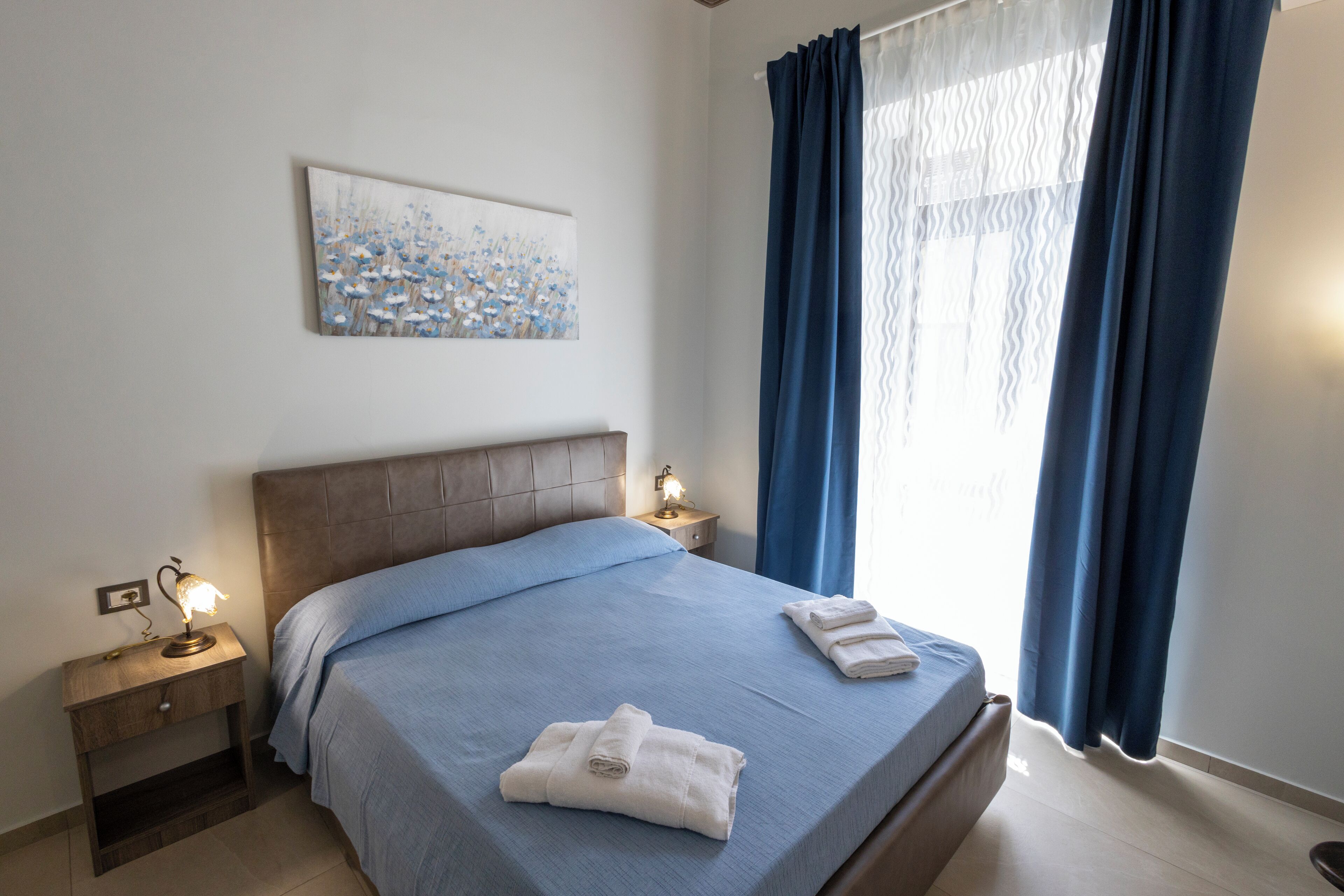 A neatly made bed with blue bedding, a bedside lamp, and a folded towel on the bed.